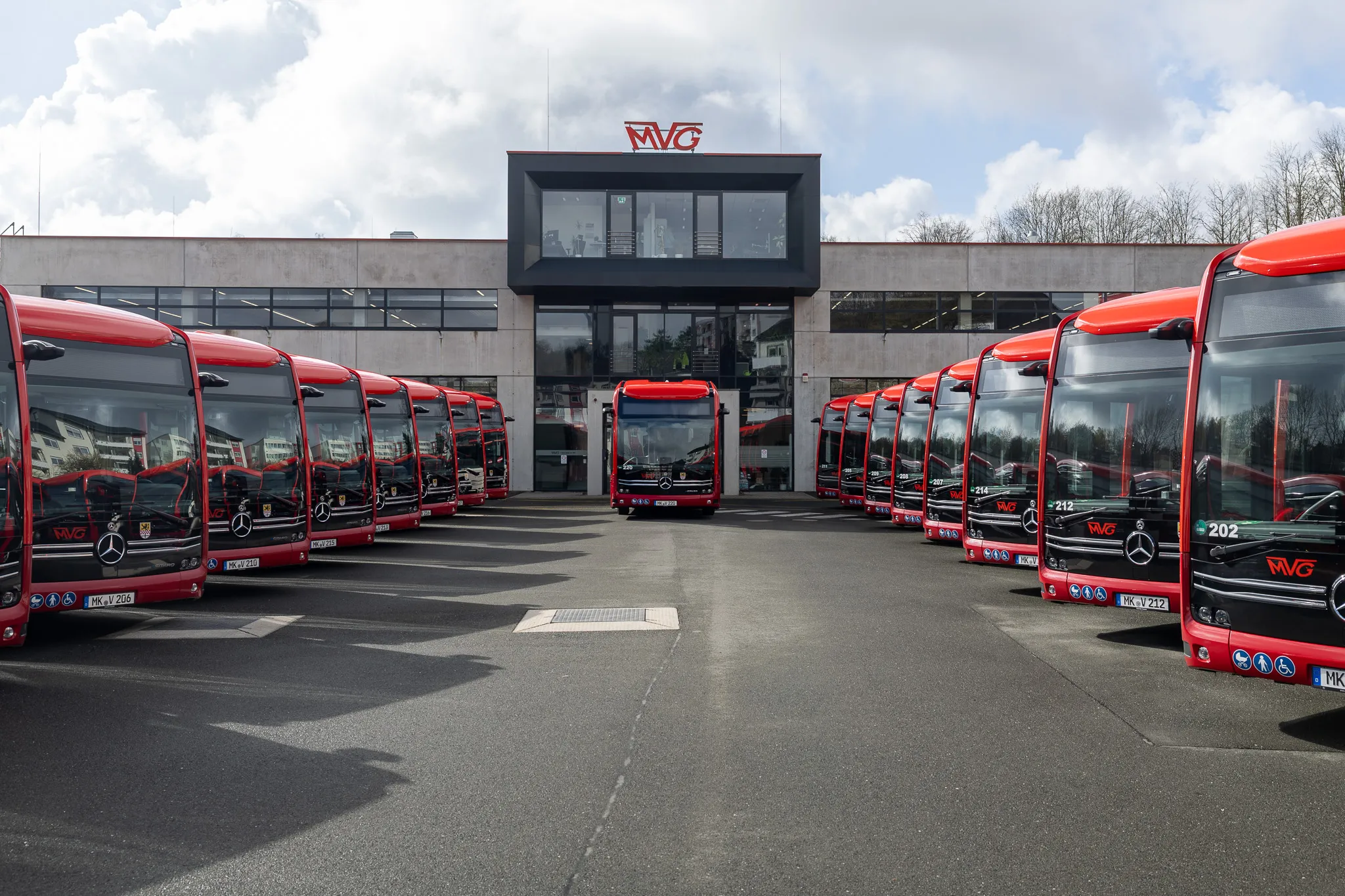 Reihe roter Elektrobusse der Münchner Verkehrsgesellschaft (MVG) vor einem modernen Gebäude mit dem MVG-Logo.