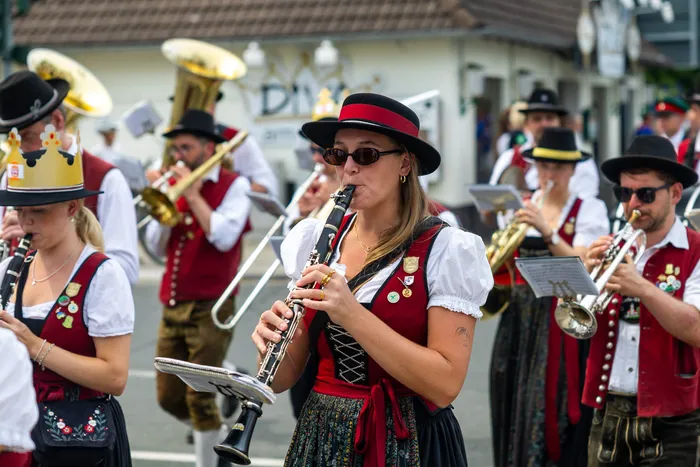 Eine Frau in traditioneller Tracht spielt eine Klarinette, während im Hintergrund weitere Musiker mit Blasinstrumenten zu sehen sind.