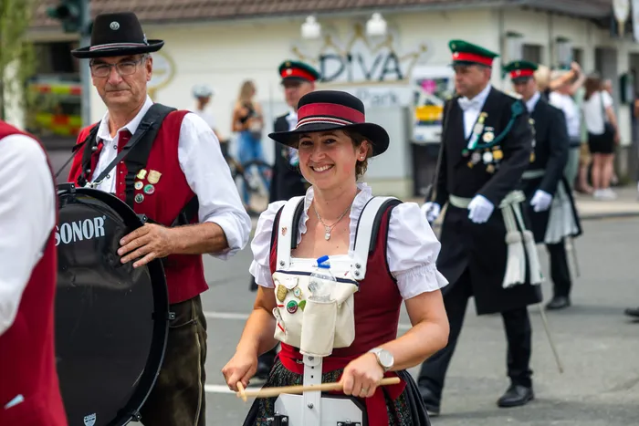 Eine lächelnde Frau in Tracht hält Trommelstöcke, während ein Mann daneben eine große schwarze Trommel spielt.