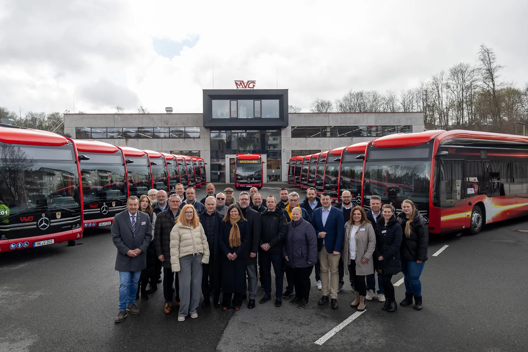 Gruppe von Menschen steht vor einer Reihe neuer roter Elektrobusse der MVG vor dem Betriebshof.