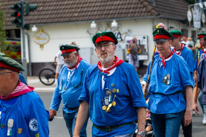 Mitglieder der Meinerzhagener Schützengilde in blauen Hemden, roten Halstüchern und grünen Kappen ziehen in einer Prozession durch die Straße.
