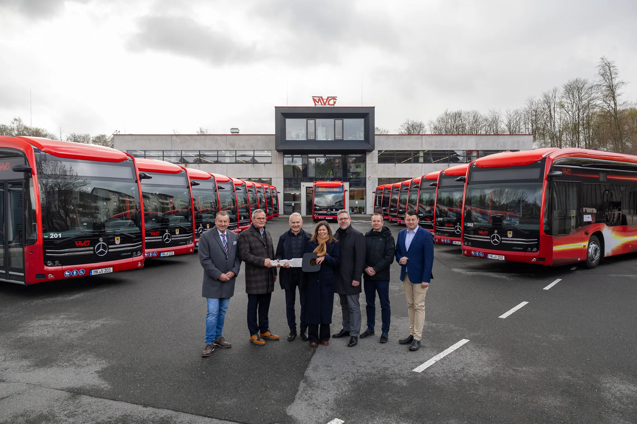 Eine Gruppe von sieben Personen steht vor einer Reihe roter Mercedes-Busse. Im Hintergrund ein modernes Gebäude mit dem MVG-Logo.