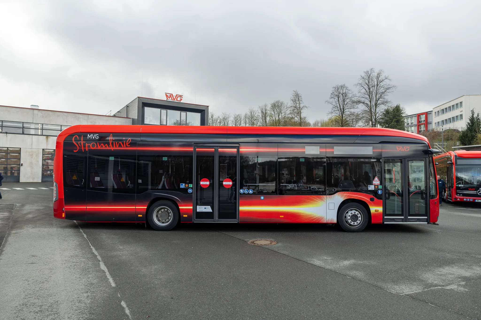 Roter Elektrobus der Münchner Verkehrsgesellschaft (MVG) mit der Aufschrift „Stromlinie“ steht auf einem Parkplatz vor einem modernen Gebäude.