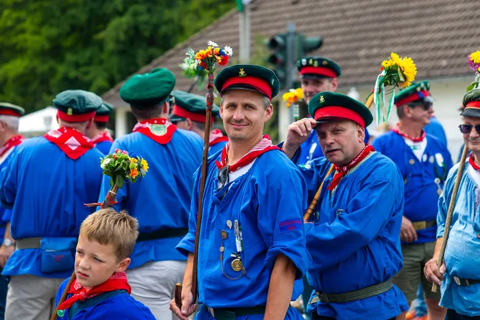 Mitglieder der Meinerzhagener Schützengilde in blauen Hemden, roten Halstüchern und grünen Kappen halten mit Blumen geschmückte Stäbe.