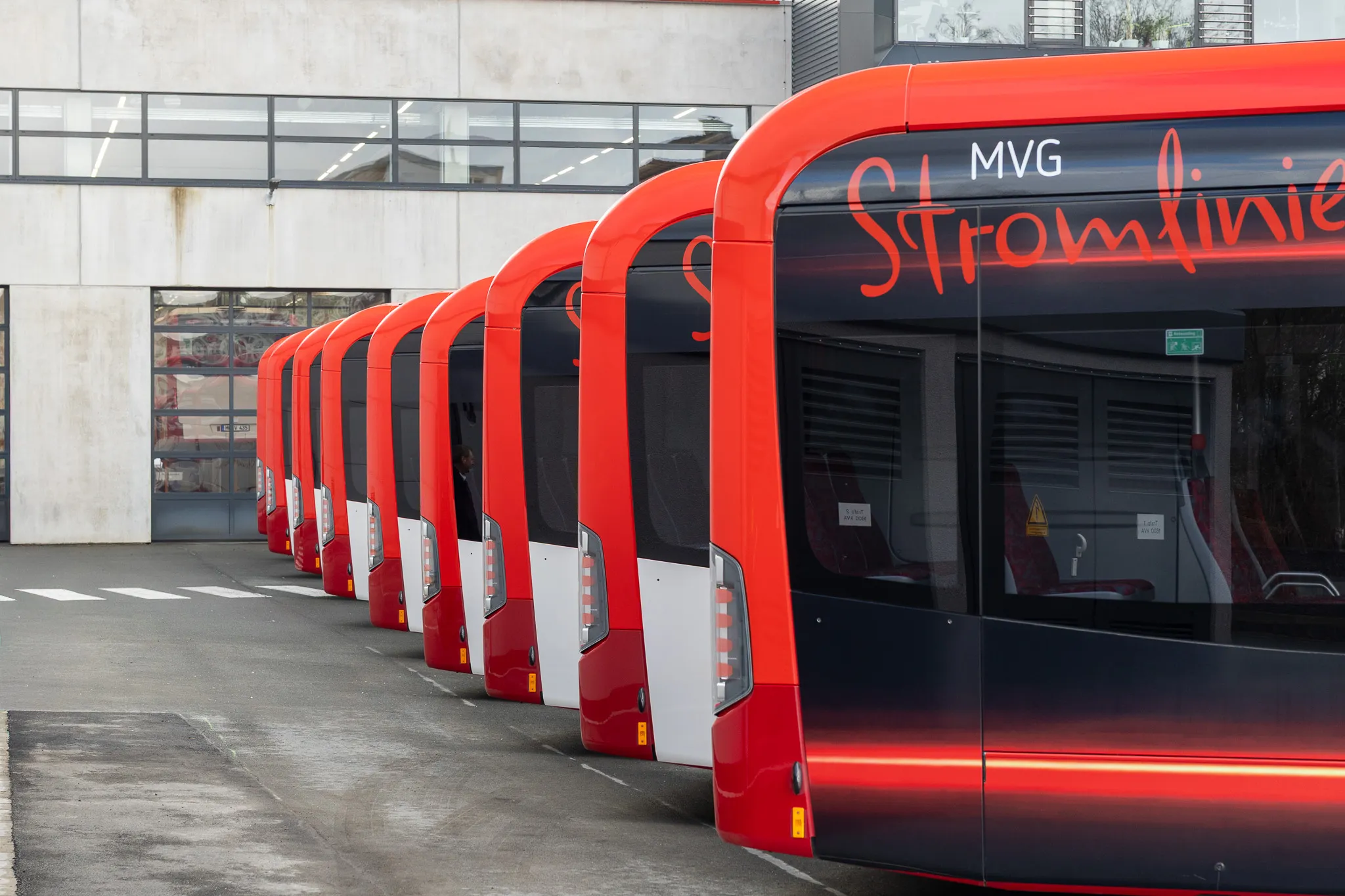 Reihe roter Elektrobusse der MVG vor einem modernen Gebäude, beschriftet mit „Stromlinien“.