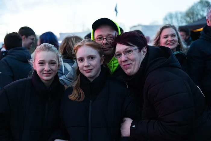 Drei Frauen und ein Mann lächeln in die Kamera, umgeben von einer Menschenmenge bei einer Veranstaltung im Freien.