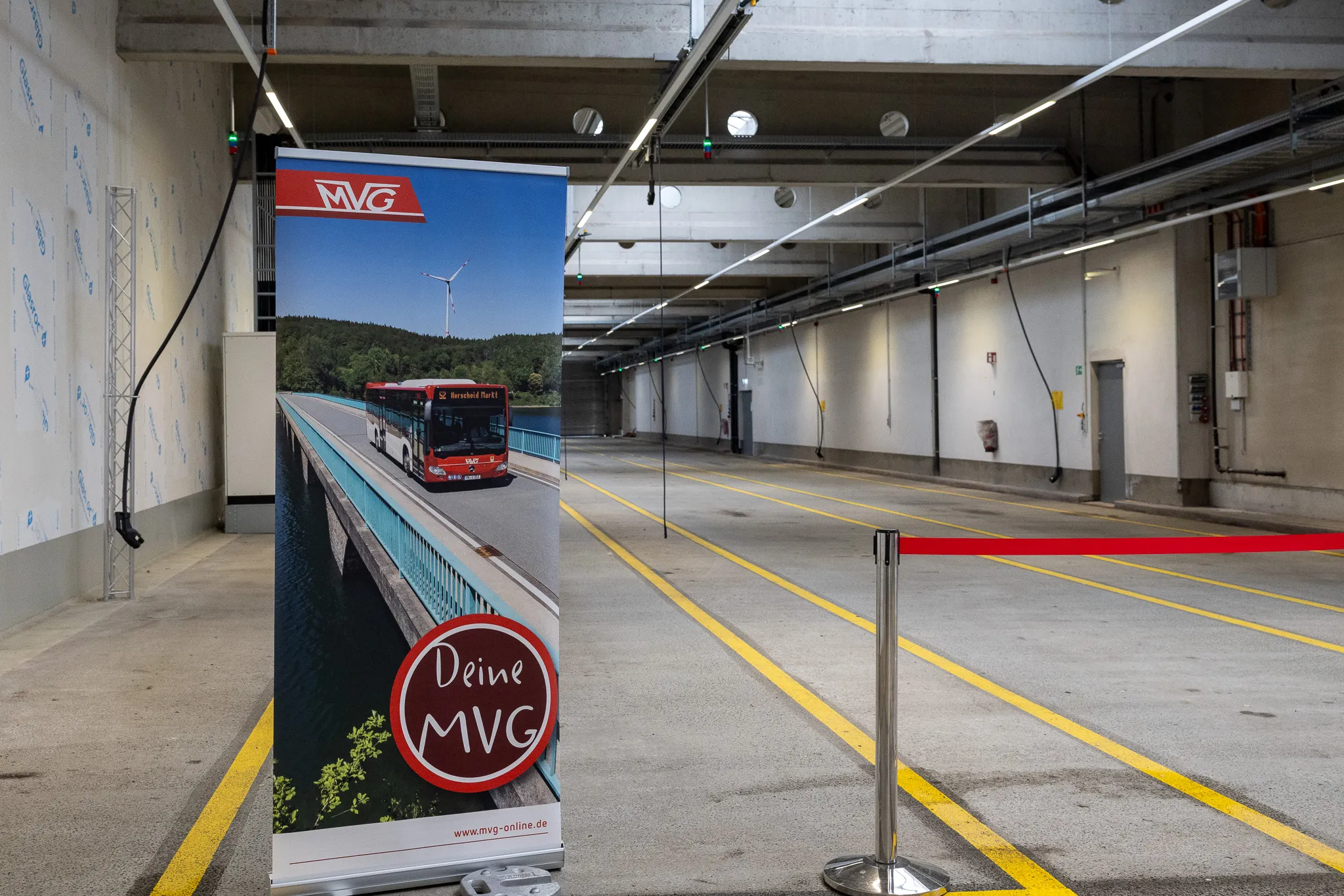 Roll-up-Banner mit einem roten MVG-Bus auf einer Brücke und dem Slogan „Deine MVG“ in einem leeren Busdepot.