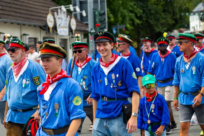 Mitglieder der Meinerzhagener Schützengilde in blauen Hemden und roten Halstüchern ziehen in einer Parade durch die Straße.