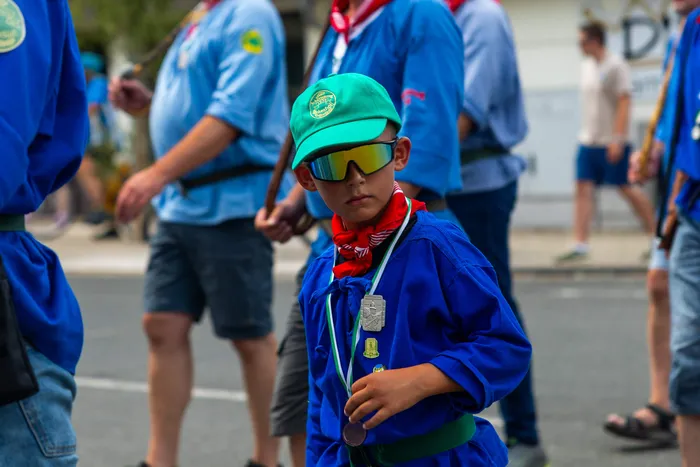 Ein Junge in blauer Uniform, grüner Kappe und gelber Sonnenbrille hält eine Medaille in der Hand.