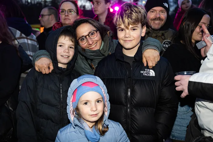 Eine Frau umarmt ihre beiden Kinder vor einer Menschenmenge bei einem Osterfeuer. Im Hintergrund sind weitere Menschen und Lichter zu sehen.