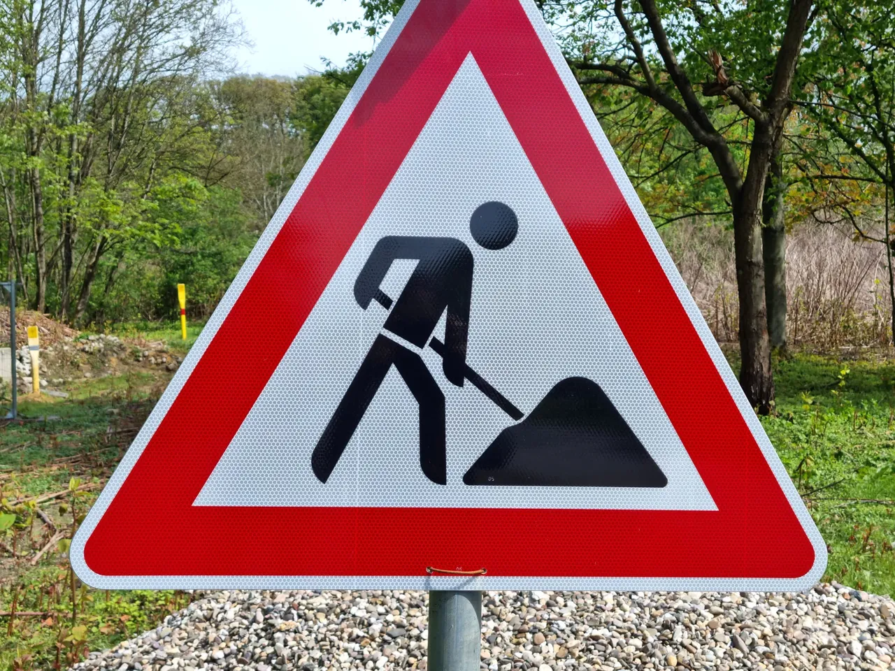Dreieckiges Warnschild für Bauarbeiten mit einer schwarzen Silhouette einer Person, die mit einer Schaufel gräbt.