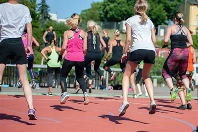 Eine Gruppe von Menschen in Sportkleidung nimmt an einem Zumba-Fitnesskurs auf einer roten Laufbahn im Freien teil.