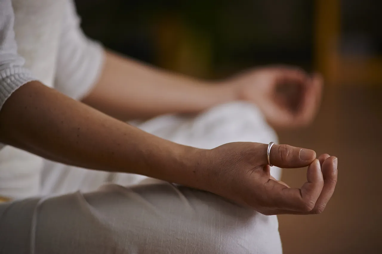 Nahaufnahme einer Person in weißer Kleidung, die ihre Hände in einer meditativen Mudra-Geste hält.