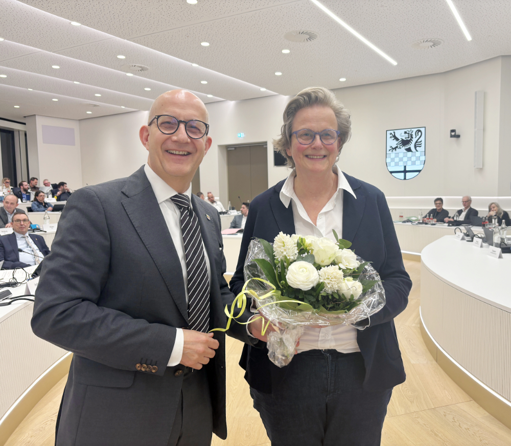 Landrat Ralf Schwarzkopf gratuliert Anja Tadday-Schlichting, die ab April neue Fachbereichsleiterin Jugend und Bildung im Märkischen Kreis wird. Sie hält einen Blumenstrauß.