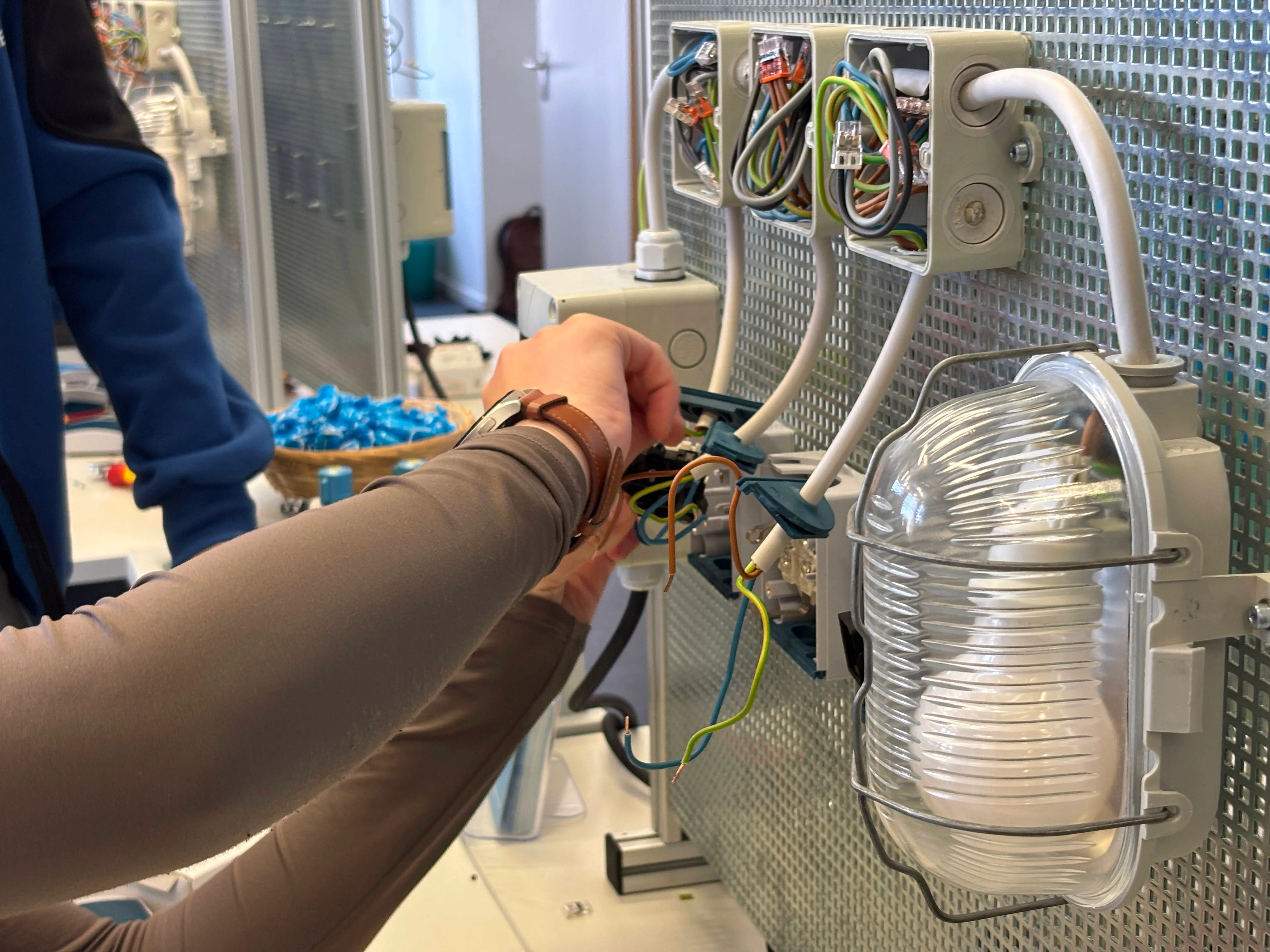 Techniker verbindet Kabel in einem Schaltkasten mit zahlreichen Anschlüssen und einem transparenten Behälter.