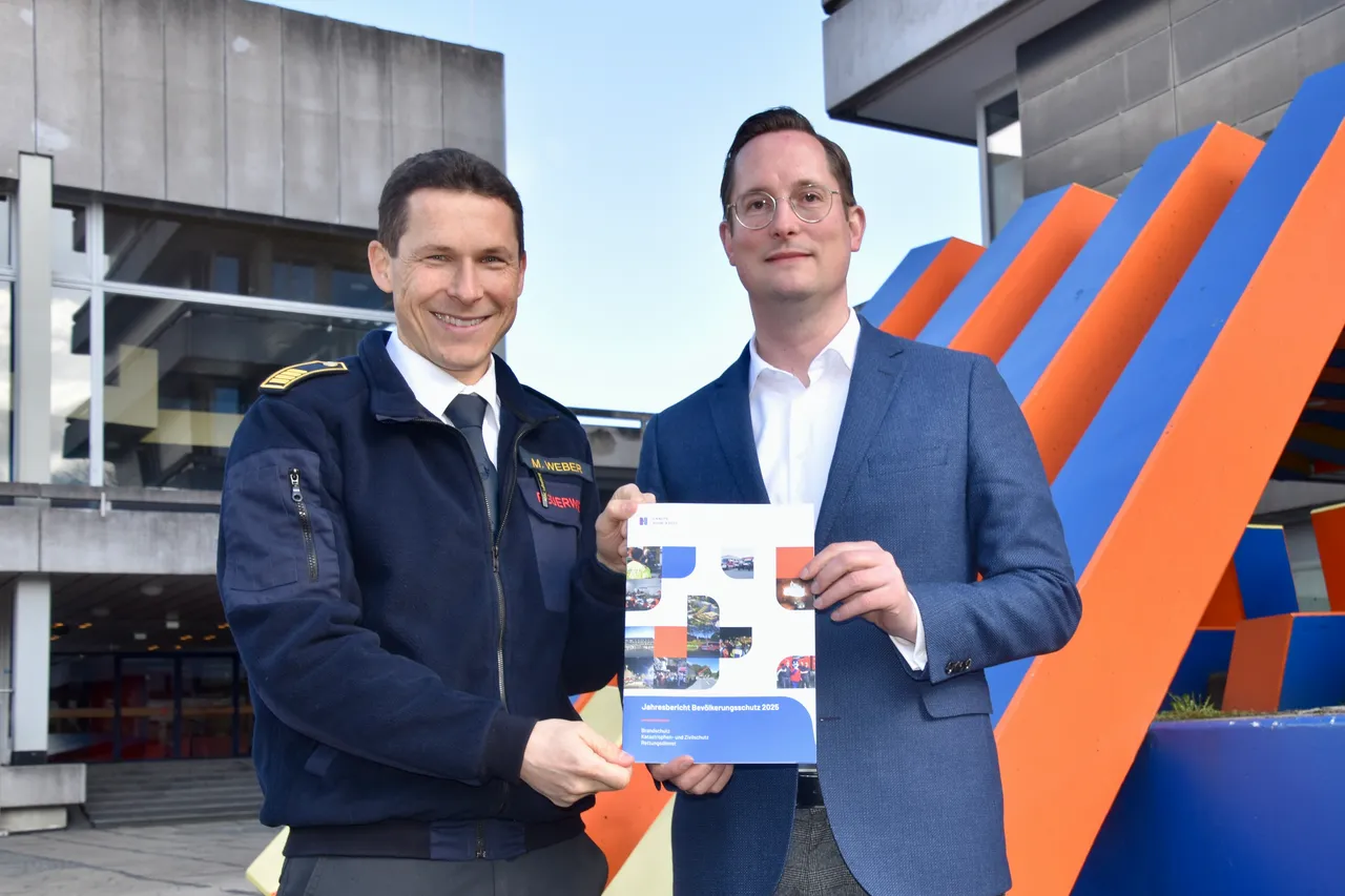 Landrat Jan-Christoph Schaberick und Martin Weber halten den Bericht „Jahrbuchbericht Bevölkerungsschutz 2023“ vor einem modernen Gebäude mit farbigen Elementen.