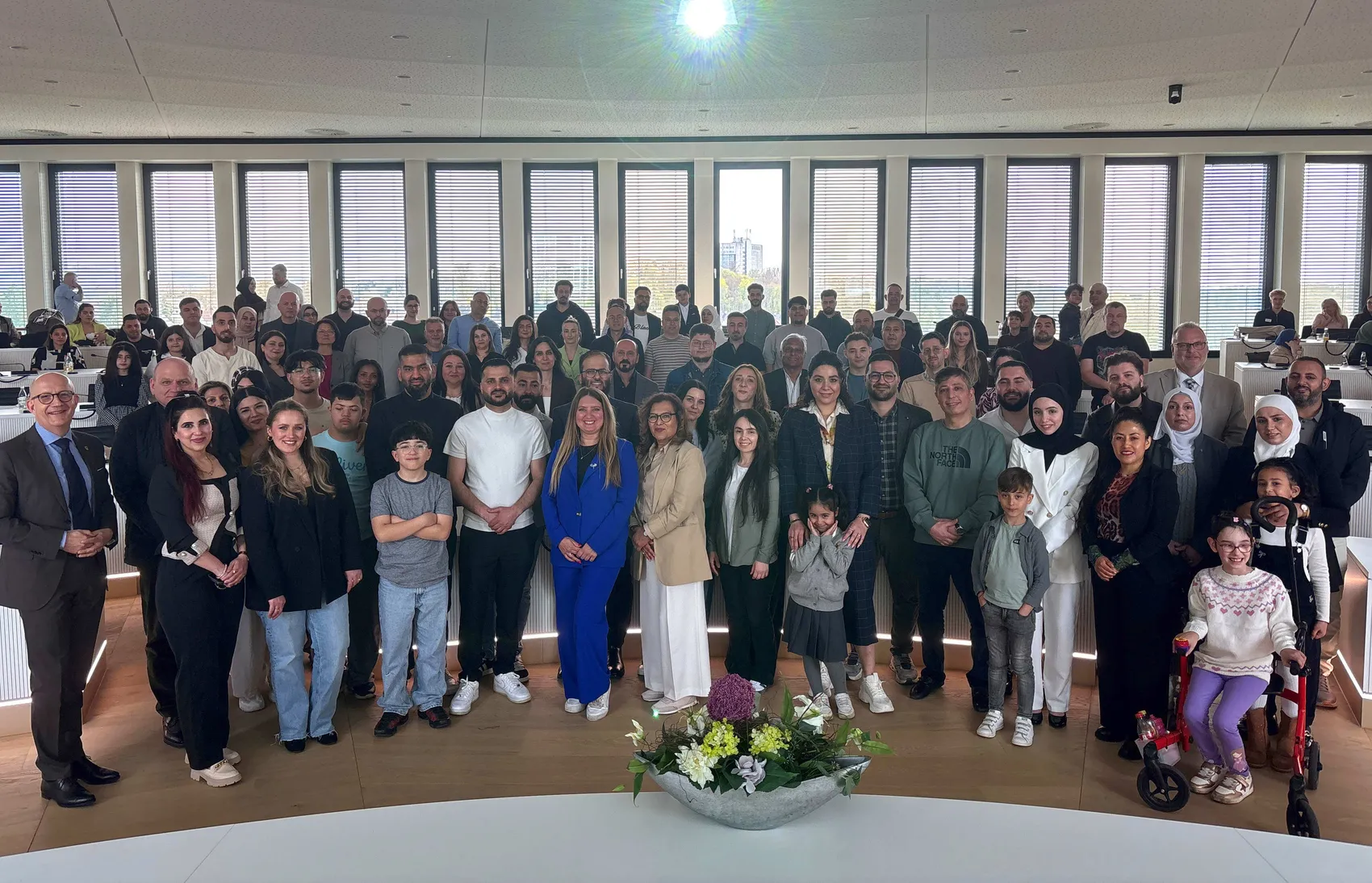 Große Gruppe von Menschen unterschiedlicher Herkunft steht im Sitzungssaal des Kreishauses Lüdenscheid zusammen, nachdem sie die deutsche Staatsbürgerschaft erhalten haben.