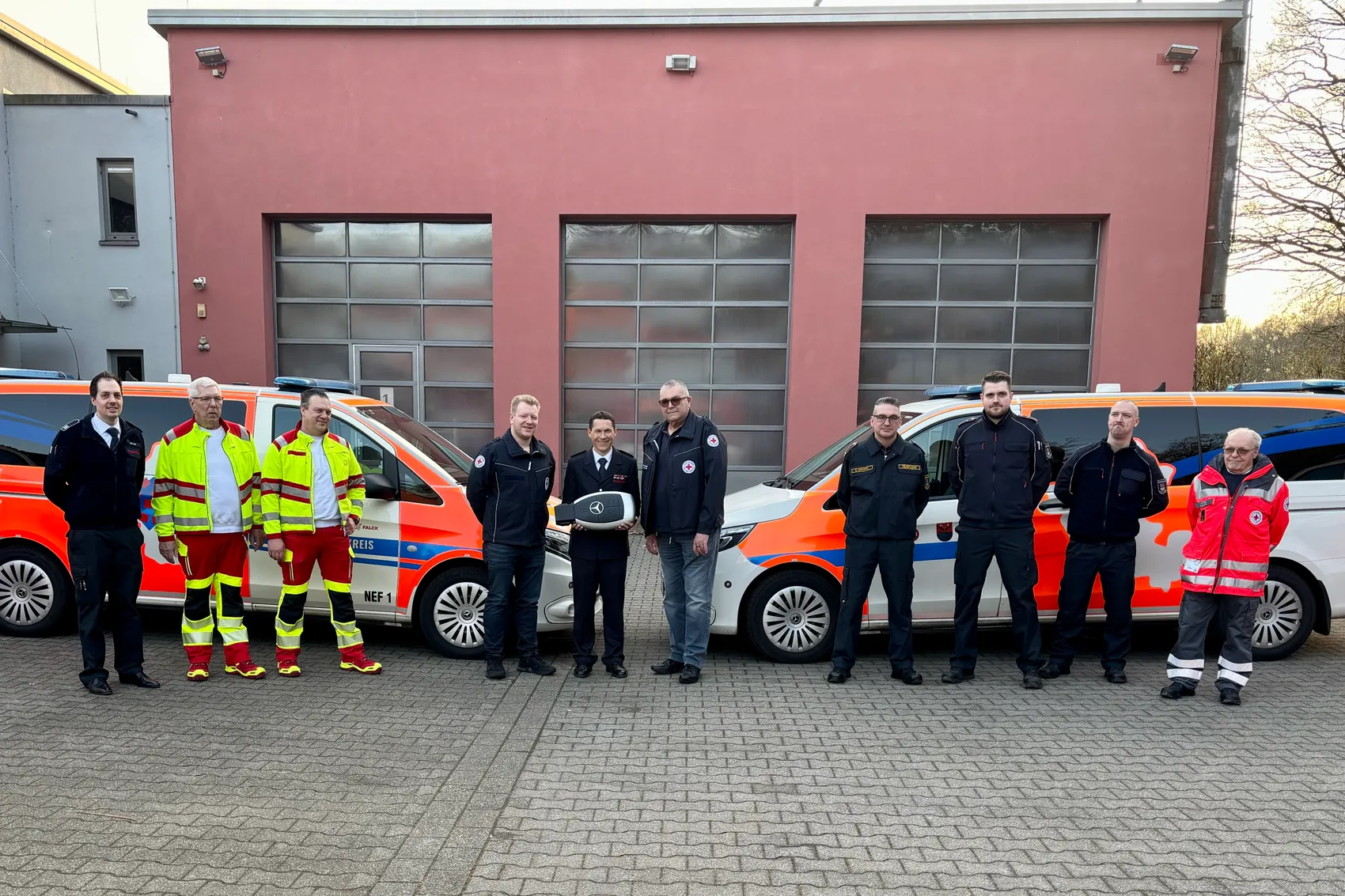 Acht Personen stehen vor einem Feuerwehrgebäude und zwei Rettungswagen. Martin Weber, Abteilungsleiter Bevölkerungsschutz und Kreisbrandmeister, übergibt symbolisch einen Schlüssel an Vertreter der Rettungsdienste und der Feuerwehr Witten.