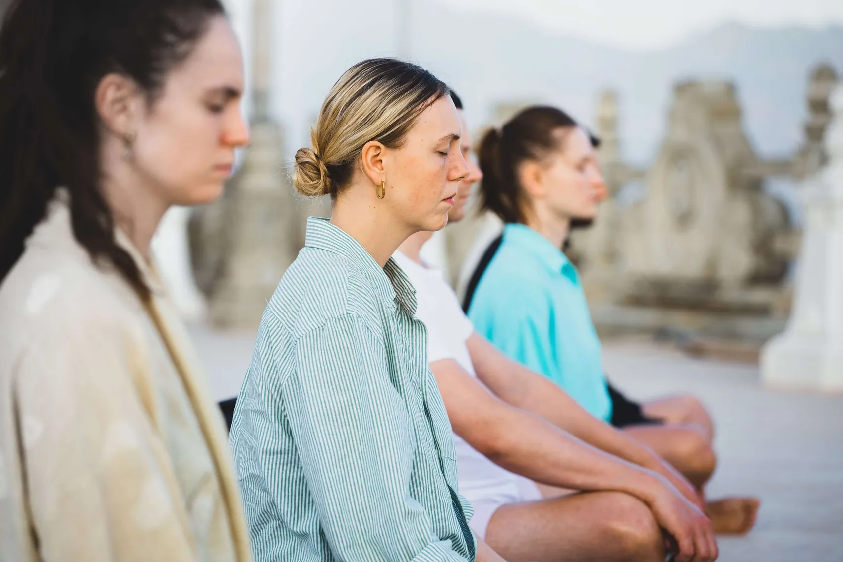 Eine Gruppe von Menschen sitzt im Freien mit geschlossenen Augen in einer Meditationshaltung.