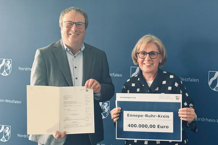 Verkehrsminister Oliver Krischer und Andrea Stöhr halten Förderbescheide hoch. Der Scheck für 400.000 Euro ist für den Ausbau des Mobilitätsangebots „FluxFux“ im Ennepe-Ruhr-Kreis.