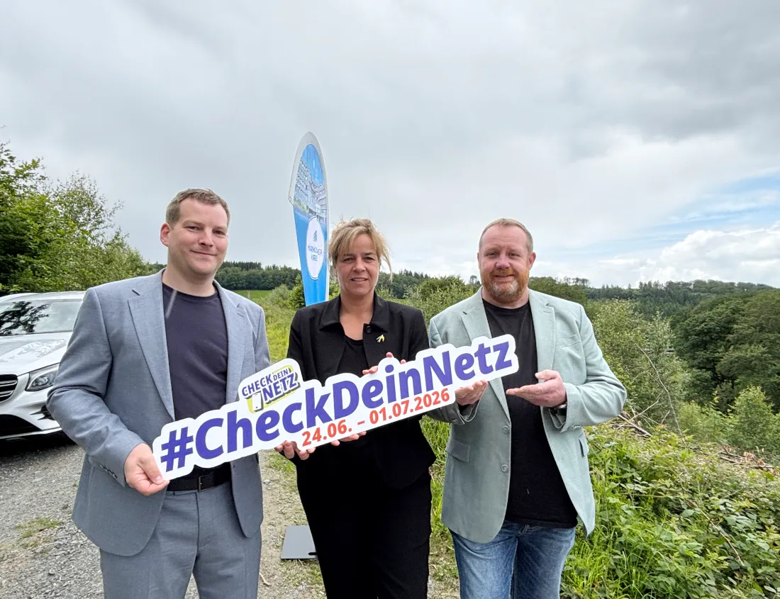 Drei Personen stehen vor einer Informationstafel mit dem Aufdruck „#CheckDeinNetz“ und einem Datumsbereich. Links steht Matthias Pohl, in der Mitte NRW-Wirtschaftsministerin Mona Neubaur und rechts Kreiskoordinator Thomas Hoheisel. Im Hintergrund sind Bäume und ein Auto zu sehen.
