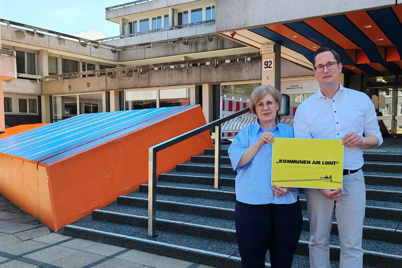 Landrat Jan-Christoph Schaberick und Kreiskämmerin Andrea Stöhr stehen vor einem Behördengebäude und halten ein Plakat mit der Aufschrift „Kommunen am Limit“ in die Kamera. Das Plakat thematisiert die schwierige finanzielle Lage der Kommunen.