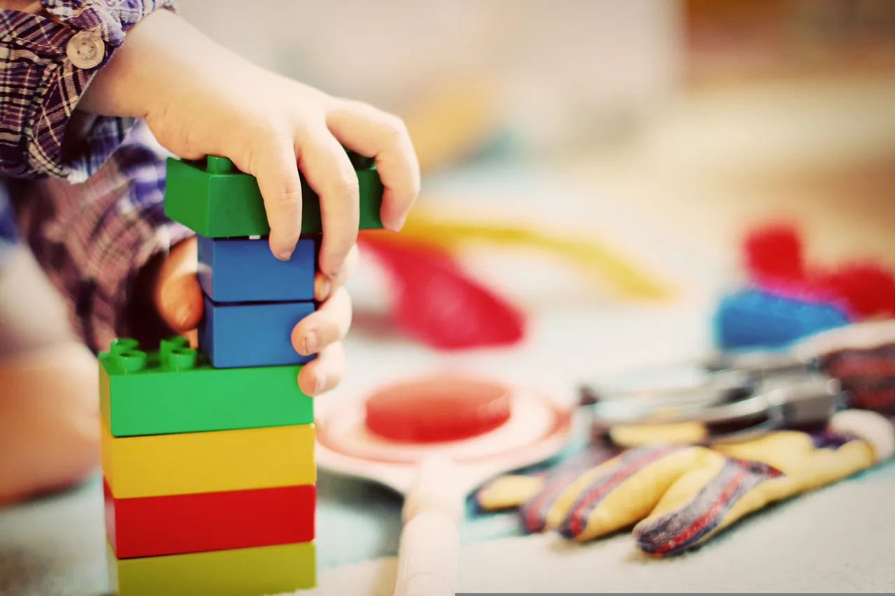 Kinderhände stapeln bunte Kunststoff-Bauklötze in Grün, Blau, Gelb und Rot übereinander.