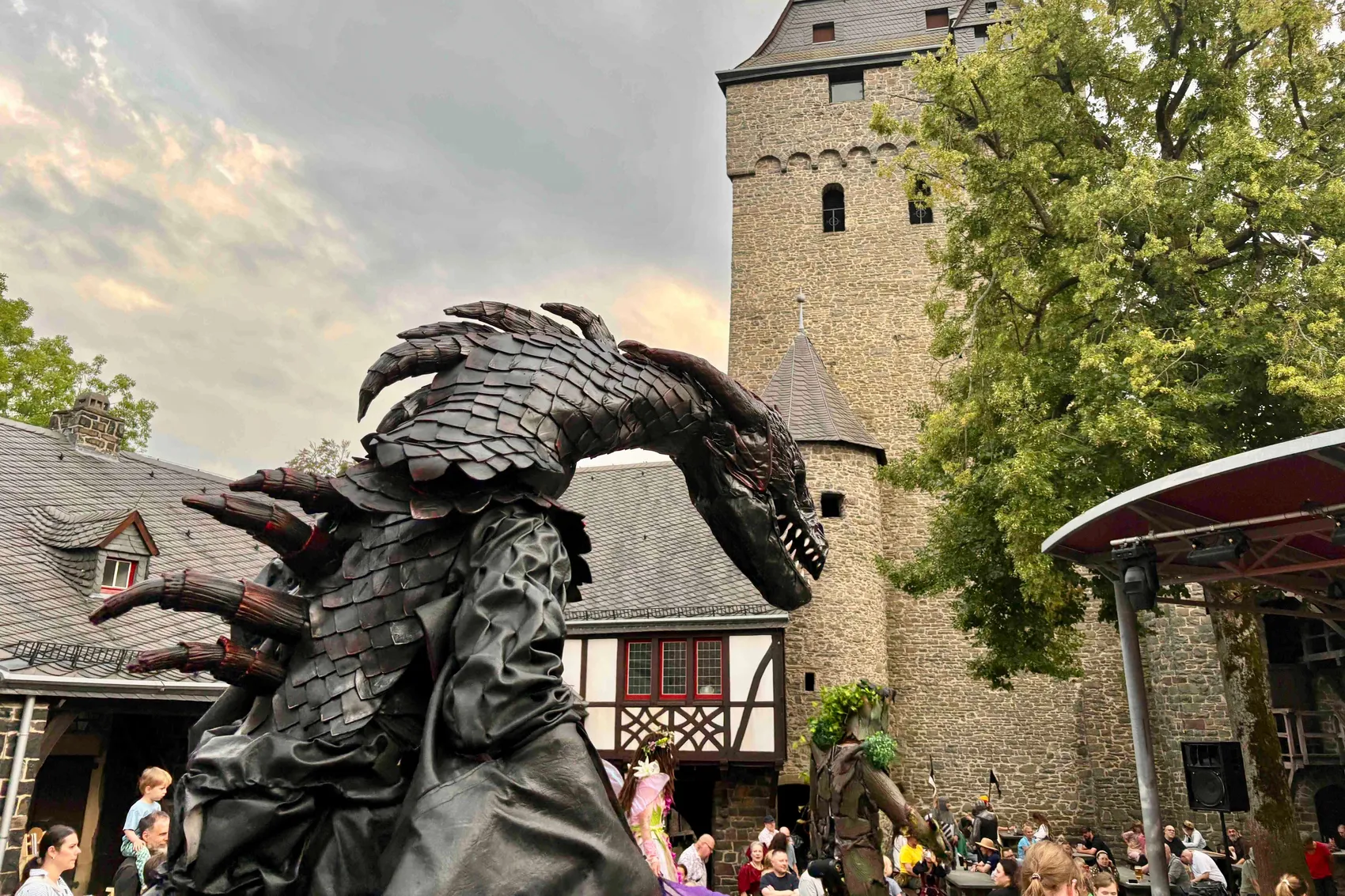 Eine große, dunkle Drachenfigur mit Schuppen vor einem Steinturm und Fachwerkhäusern auf Burg Altena.