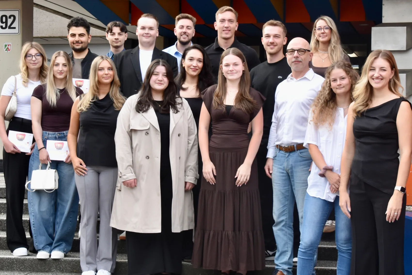 Eine Gruppe von etwa vierzehn Personen posiert gemeinsam auf einer Treppe vor einem Gebäude.