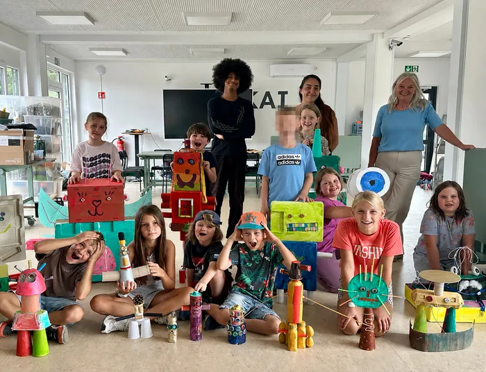 Kinder und Erwachsene posieren mit ihren bunten, aus Recyclingmaterialien gebastelten Müllmonstern.