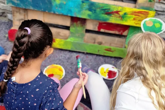 Zwei Kinder bemalen eine Europalette mit bunten Farben.