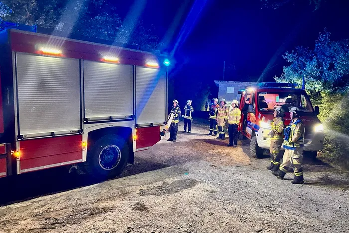 Feuerwehrleute in Schutzkleidung stehen nachts bei einem Einsatz zwischen einem großen Löschfahrzeug und einem kleineren Einsatzwagen.