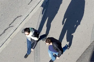 Zwei Personen gehen auf einem Gehweg und werfen lange Schatten.