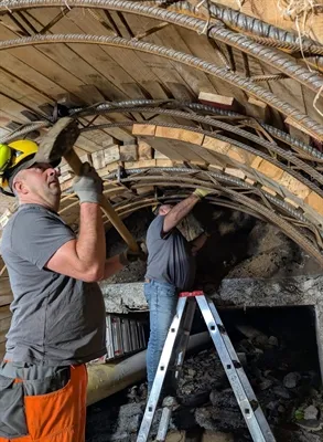 Bauarbeiter montieren Stahlbögen und Holzverstrebungen zur Sicherung eines Stollens.