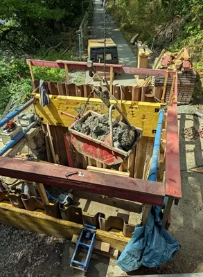 Ein mit Betonbruch gefüllter Metallbehälter wird an einer Baustelle über einer Schalung transportiert.