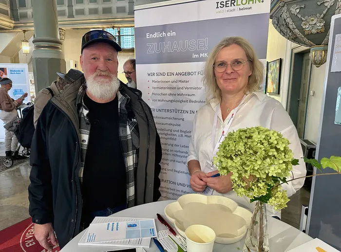 Norbert Hellmann und Tatjana Hegmann-Thomas stehen hinter einem Tisch mit Broschüren vor einem Plakat zum Thema Wohnraum.