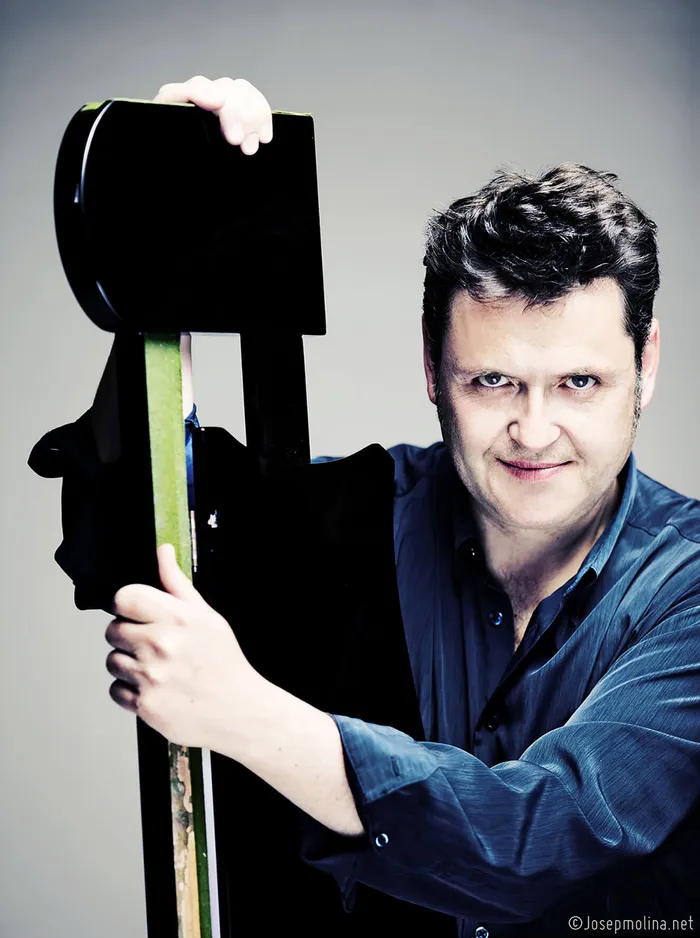 Paul Rivinius hält ein großes schwarzes Streichinstrument vor einem neutralen Hintergrund.