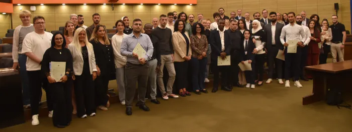 Eine große Gruppe von Männern und Frauen posiert in einem Saal und hält teilweise Urkunden.