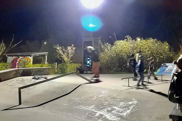 Personen nutzen nachts die Rampen und Schienen in einem hell beleuchteten Skatepark.