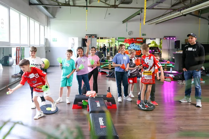 Eine Gruppe von Kindern und Jugendlichen nimmt an einem Workshop in einer Turnhalle teil. Ein Junge wirft einen Ball, während andere zusehen und ein Trainer im Hintergrund steht.