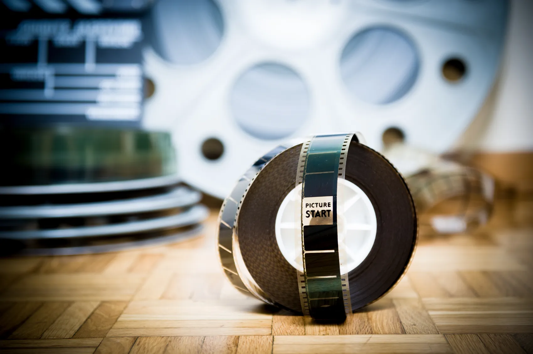 Ein Filmstreifen mit der Aufschrift „PICTURE START“ liegt vor mehreren Filmrollen auf einem Holzboden.