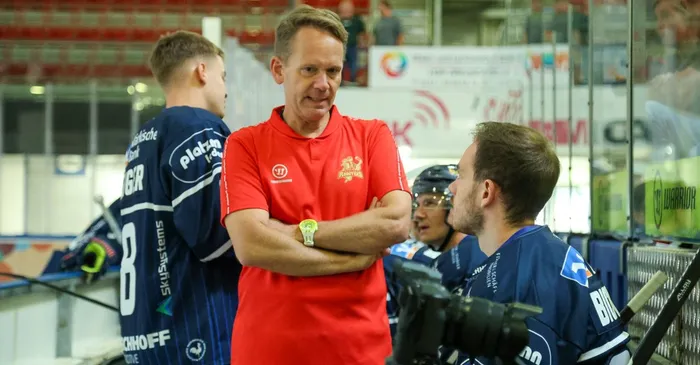 Dr. Jochen Veit im roten Poloshirt spricht mit Kevin Bicker im blauen Eishockeytrikot während eines Trainings.