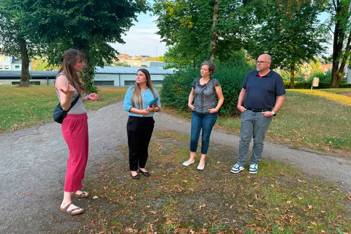 Vier Personen stehen im Gespräch auf einem Weg in einer Parkanlage vor Bäumen und Gebäuden.