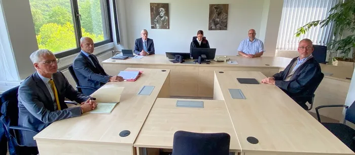 Sechs Personen sitzen an einem U-förmigen Konferenztisch in einem hellen Besprechungsraum.