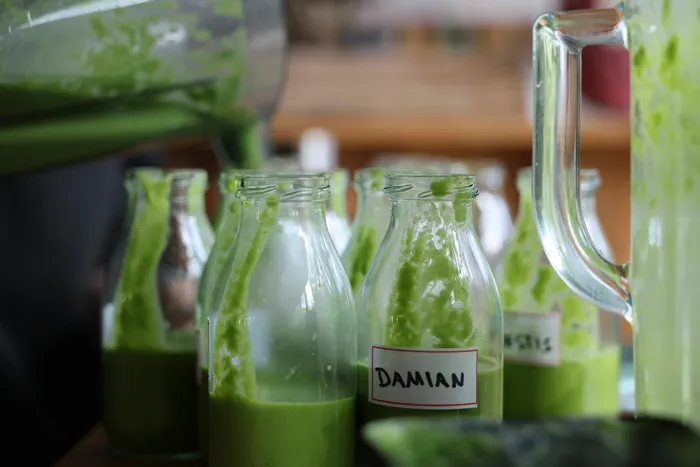 Grüne Smoothies werden aus einem Mixer in Glasflaschen gefüllt, eine davon ist mit „Damian“ beschriftet. Der Workshop vermittelte Kindern gesunde Ernährung.