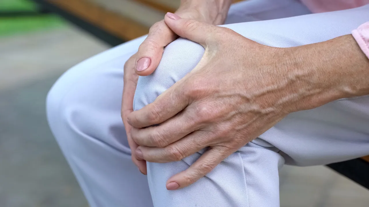 Eine Person hält sich mit beiden Händen das Knie.