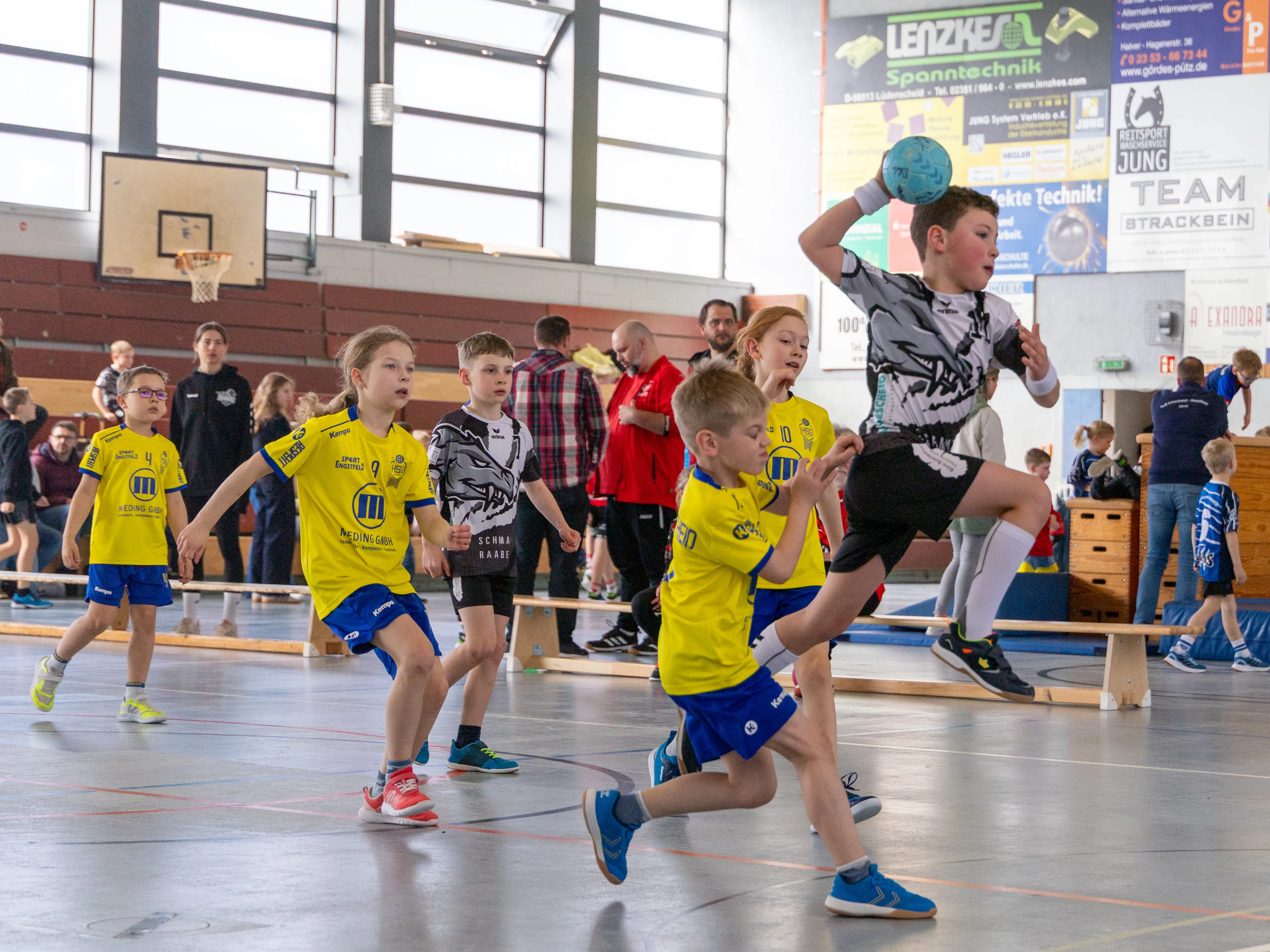 Handballspieler der F-Jugend der SGSH Dragons im Spiel, ein Spieler springt zum Wurf, während andere versuchen, den Ball zu erobern.