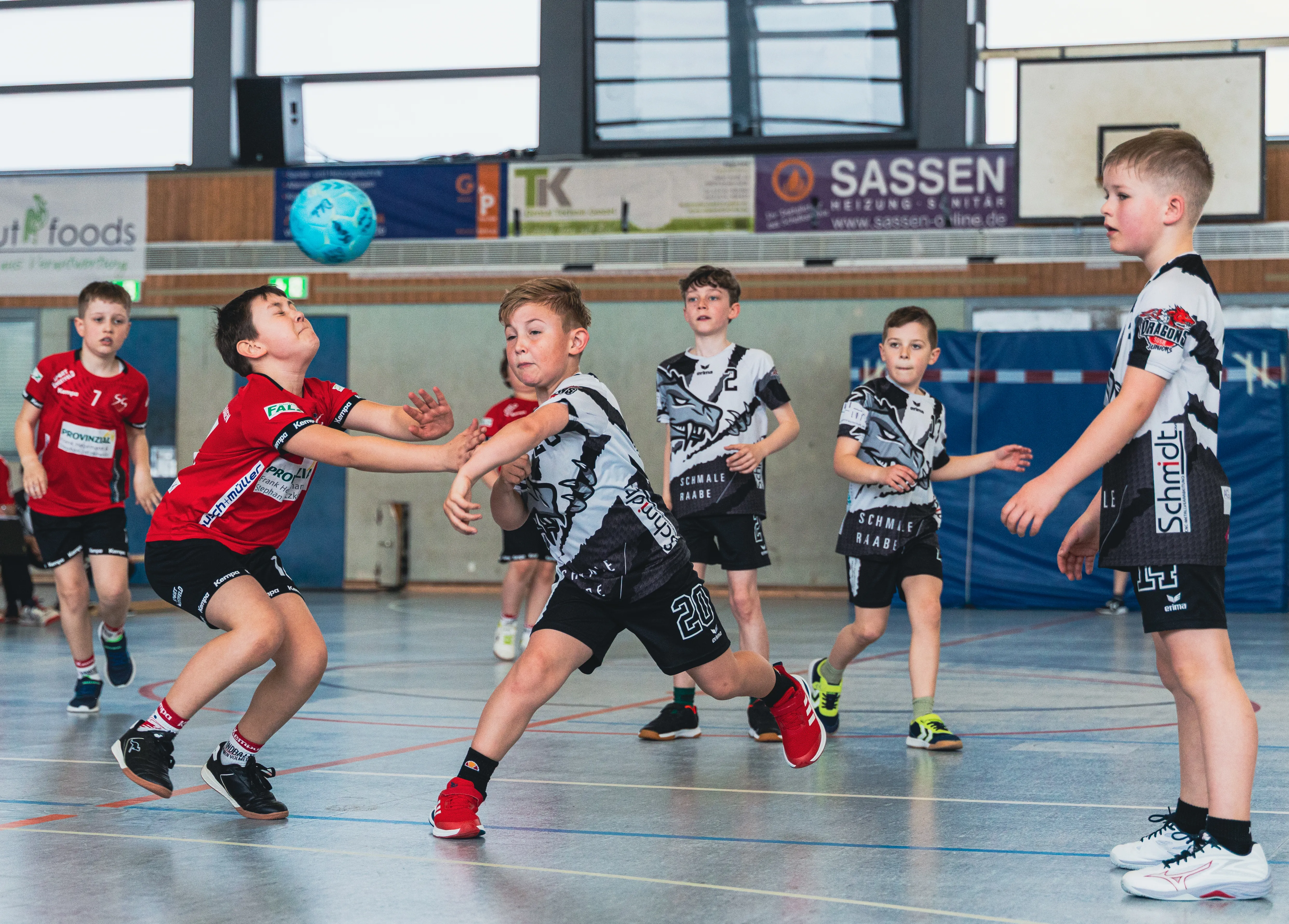 Handballspieler der F-Jugend im roten und schwarz-weißem Trikot während eines Spiels in einer Sporthalle.