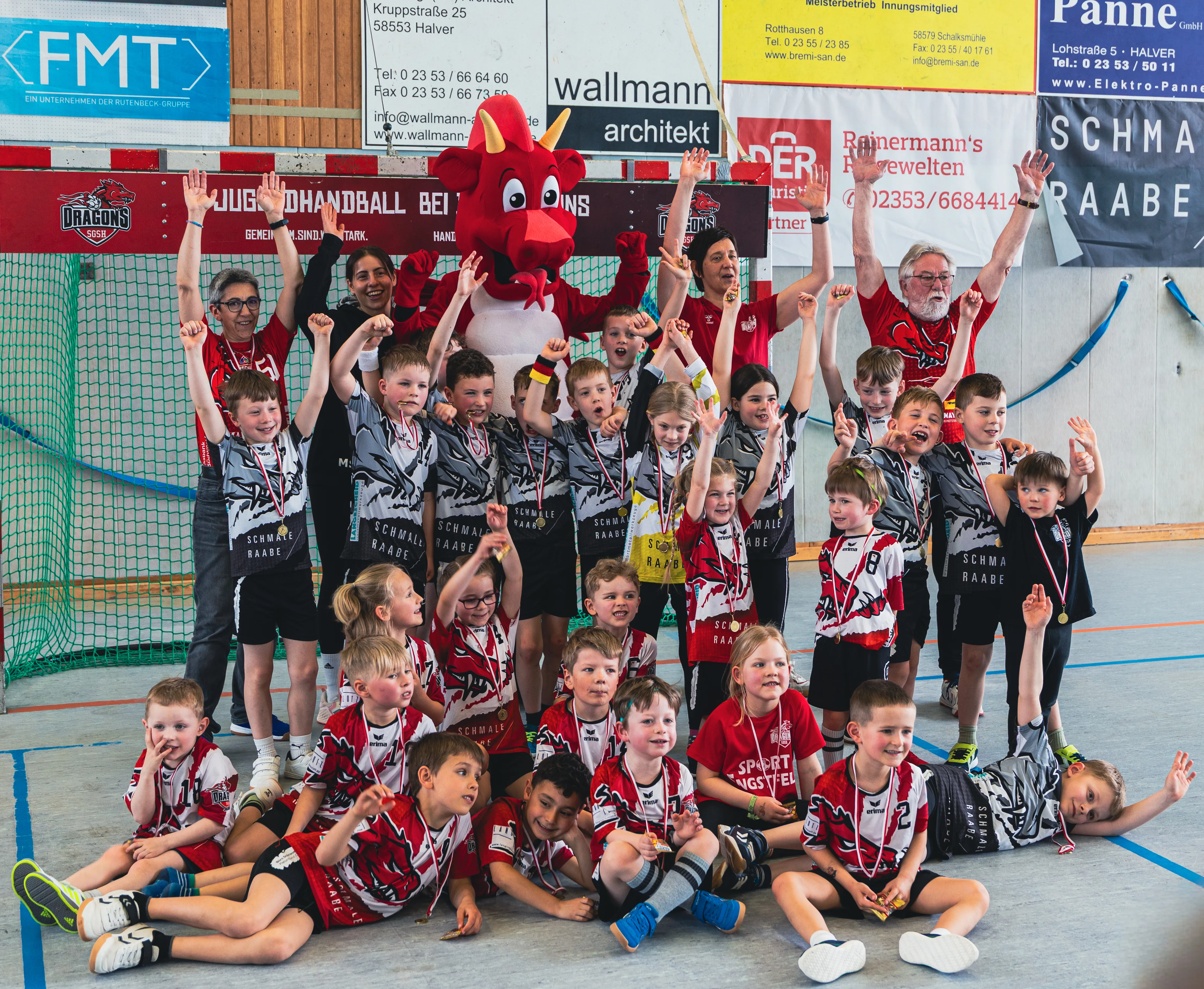 Mannschaft der F-Jugend SGSH Dragons mit Trainern und Betreuern jubelt nach einem Spiel in einer Sporthalle.