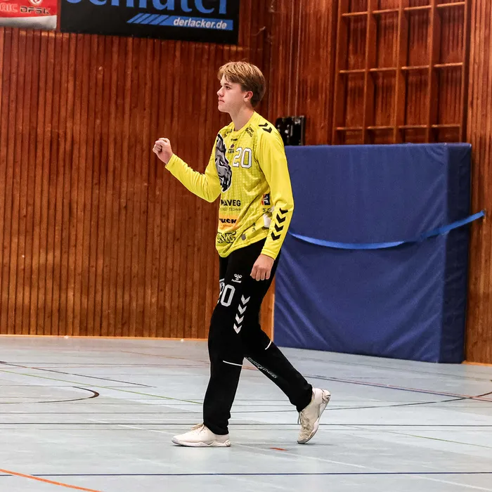 Ein Spieler der SGSH Dragons in gelbem Trikot und schwarzer Hose mit der Nummer 20 geht durch eine Sporthalle.